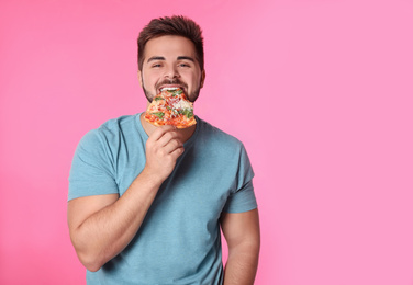 Handsome man with pizza on pink background, space for text