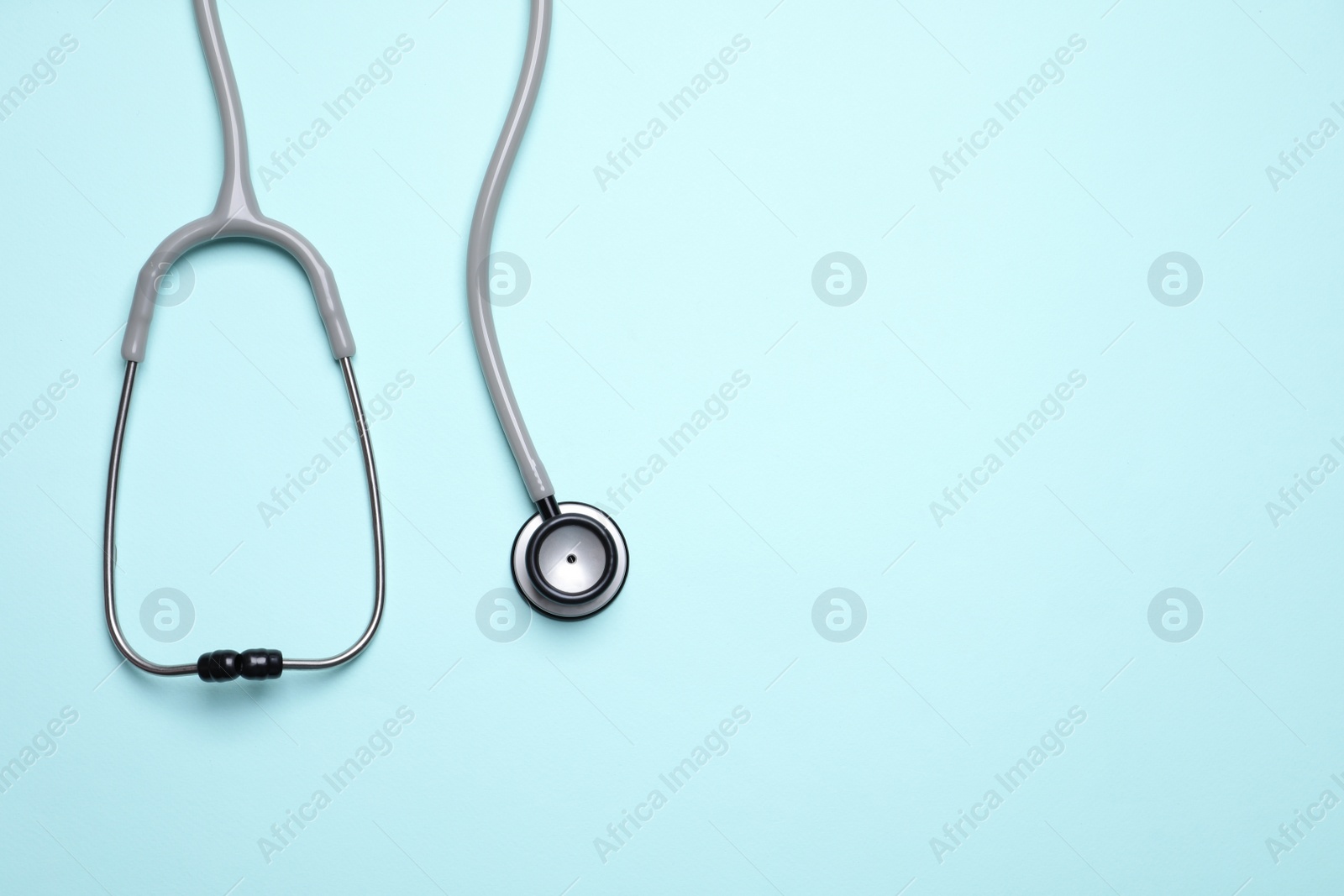 Photo of Stethoscope on light blue background, top view. Space for text