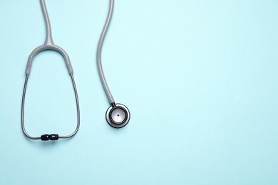 Stethoscope on light blue background, top view. Space for text