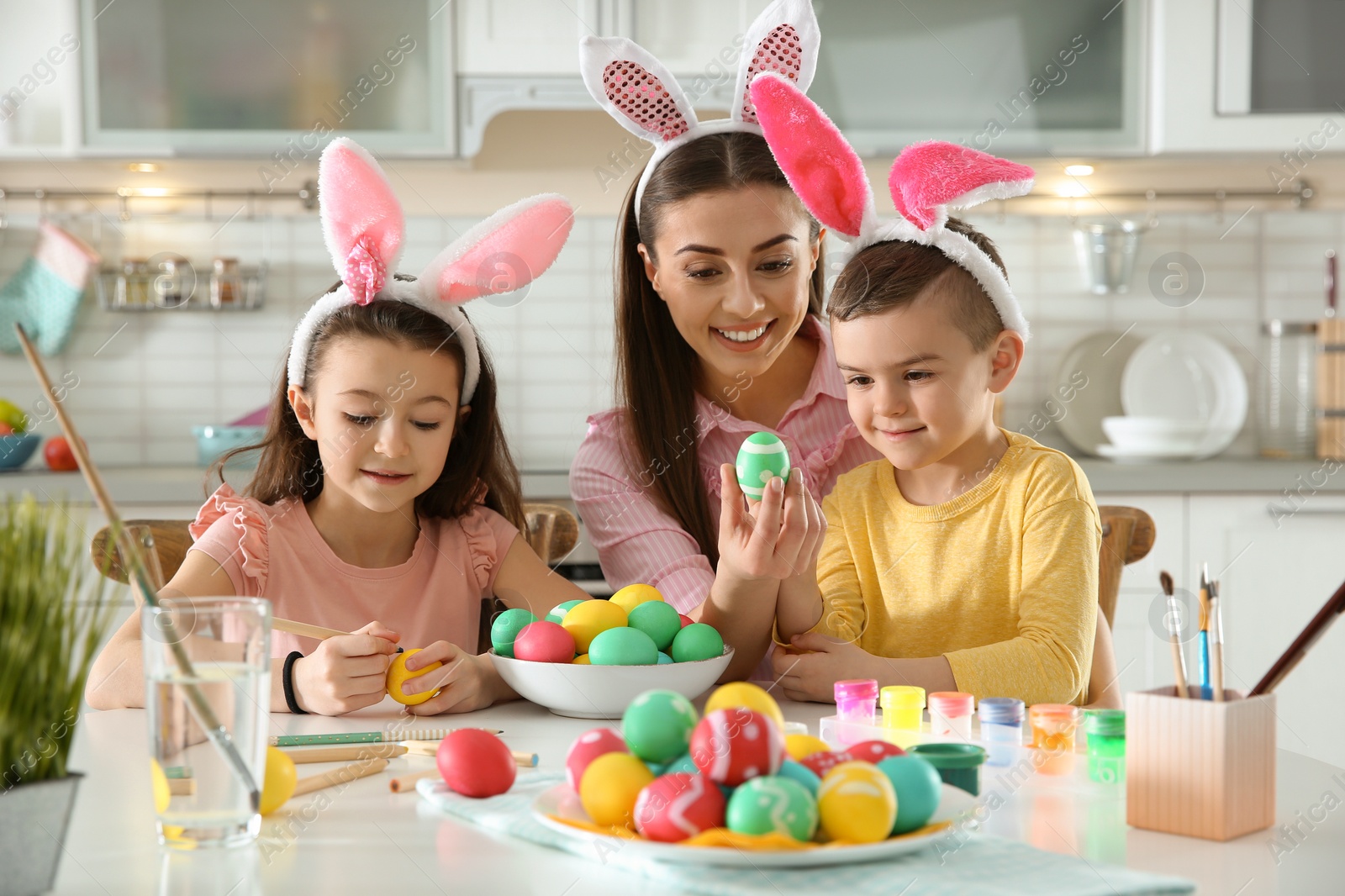 Photo of Mother and her children with bunny ears headbands painting Easter eggs in kitchen