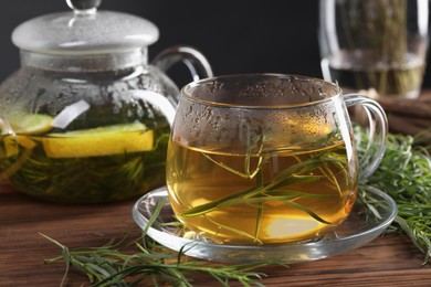 Photo of Homemade herbal tea and fresh tarragon leaves on wooden table, closeup
