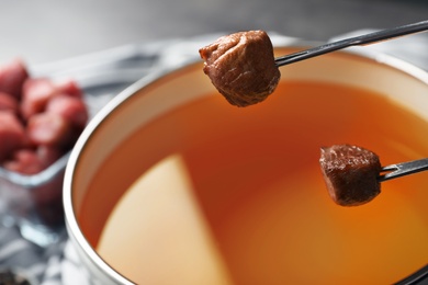 Photo of Dipping meat into fondue pot with oil on table, closeup