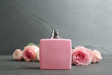 Photo of Bottle of perfume with beautiful roses on table