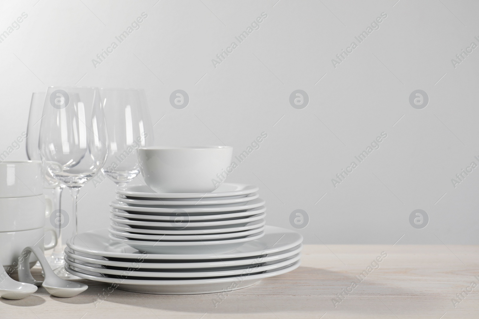 Photo of Set of clean dishware and glasses on white wooden table against light background. Space for text