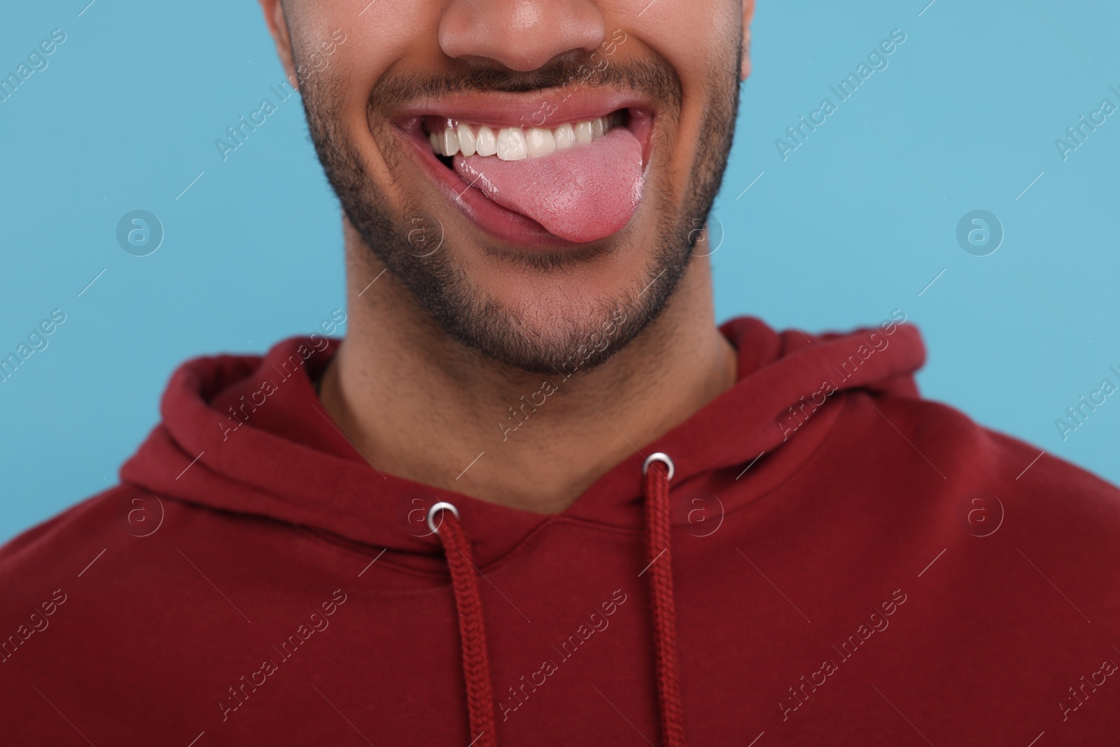 Photo of Happy man showing his tongue on light blue background, closeup