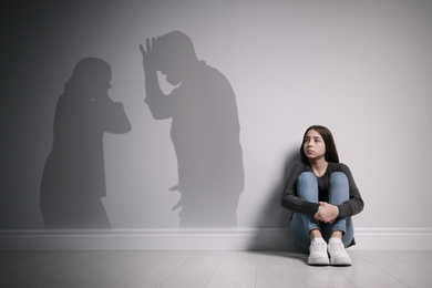 Upset teenage girl sitting on floor near wall and silhouettes of arguing parents 