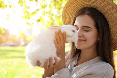 Happy woman holding cute white rabbit in park