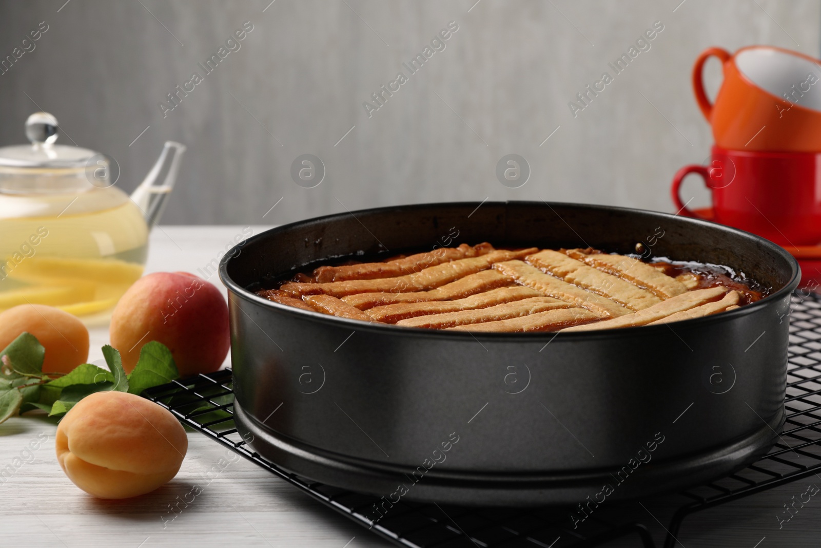 Photo of Delicious apricot pie in baking dish and fresh fruits on white wooden table