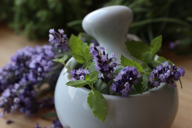 Mortar with fresh lavender flowers, mint and pestle on table, closeup