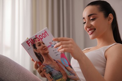 Photo of Happy young woman reading modern magazine indoors