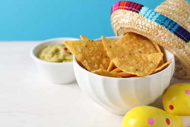 Mexican sombrero hat, nachos chips, guacamole and maracas on white wooden table