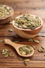 Photo of Bowls and spoon with peeled pumpkin seeds on wooden table