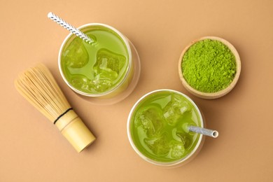 Delicious iced green matcha tea, powder and bamboo whisk on pale brown background, flat lay