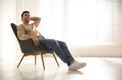 Photo of Young man relaxing in armchair near window at home. Space for text