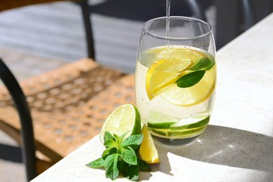 Photo of Pouring water into glass with lemon slices and mint at light grey table. Space for text