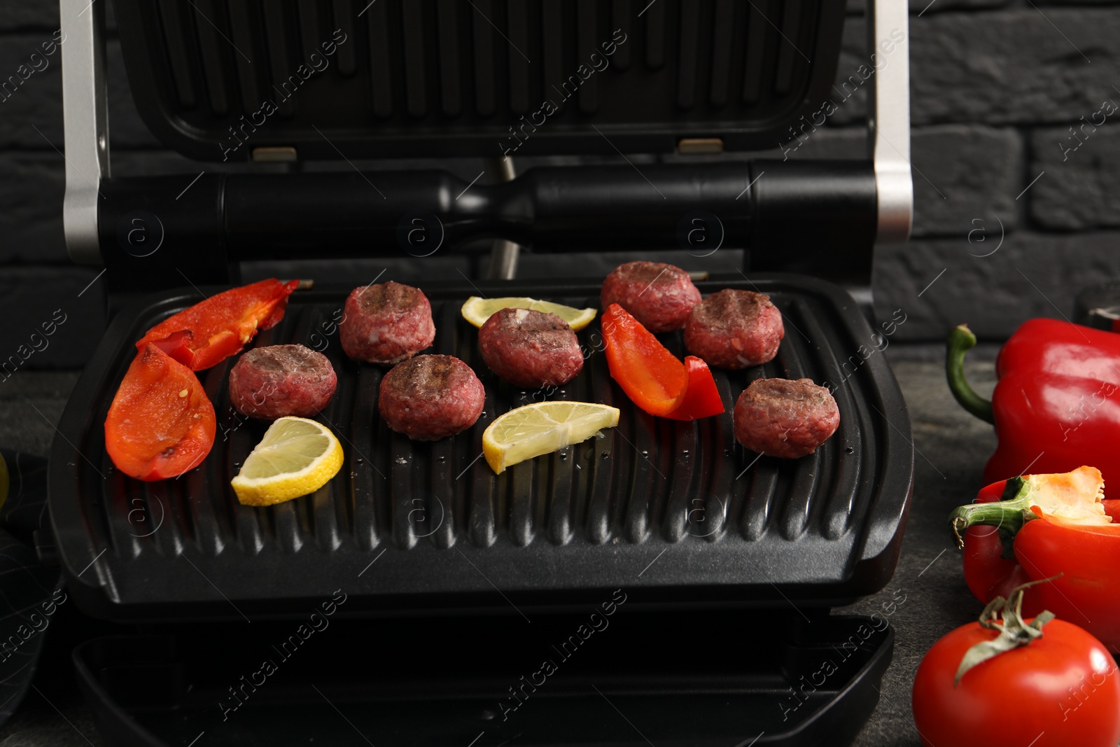 Photo of Electric grill with meat balls, bell peppers and lemon on grey table, closeup