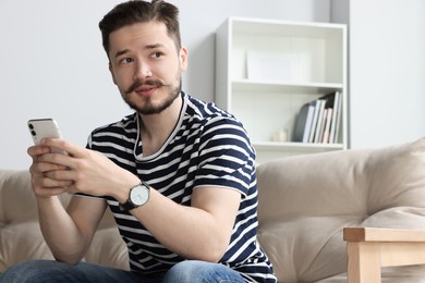 Man with smartphone on beige sofa in cozy room. Space for text