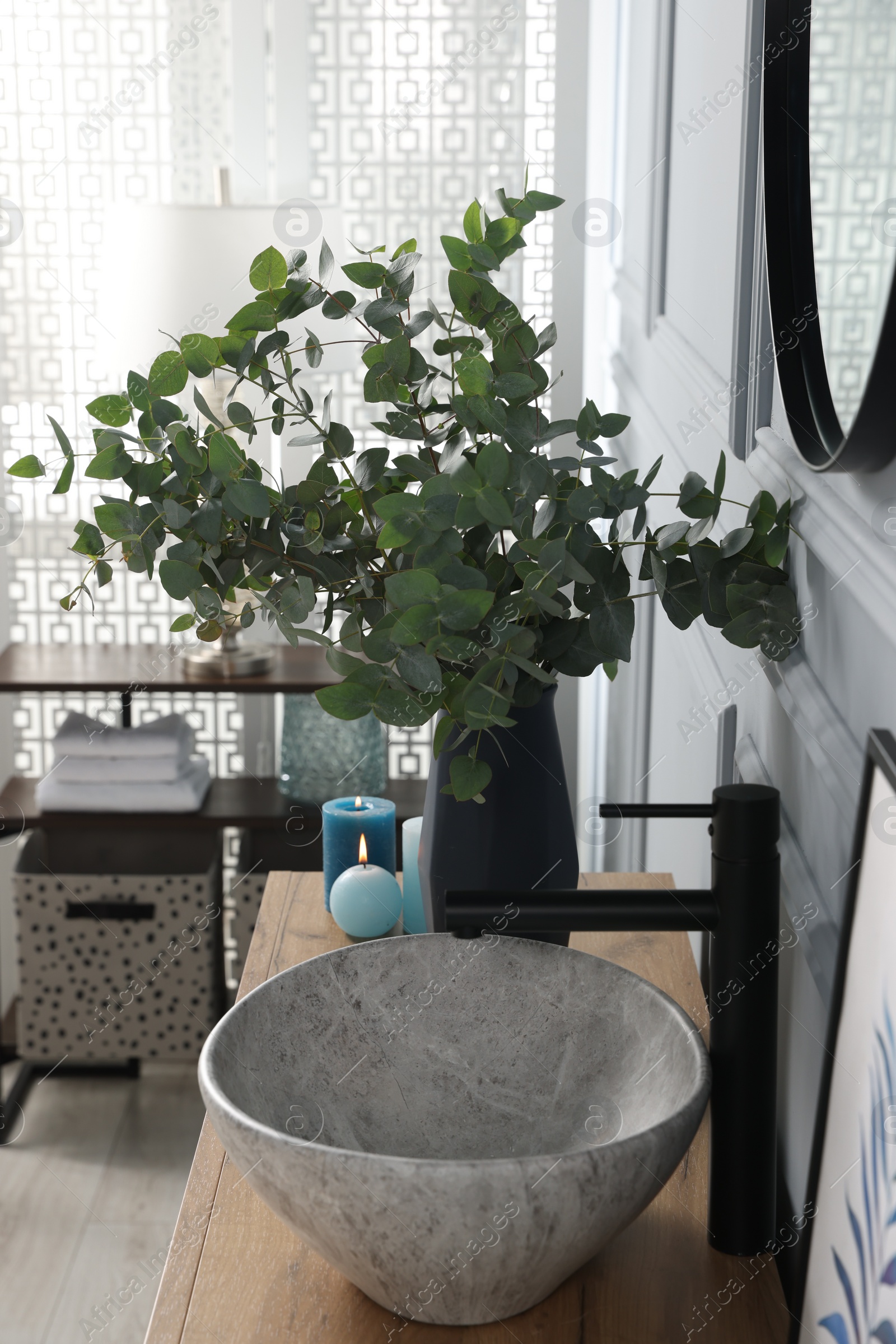 Photo of Eucalyptus branches near vessel sink on bathroom vanity. Interior design