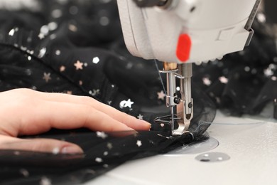 Photo of Dressmaker sewing new dress with machine in atelier, closeup