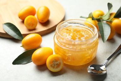 Photo of Delicious kumquat jam in jar and fresh fruits on light grey table, space for text