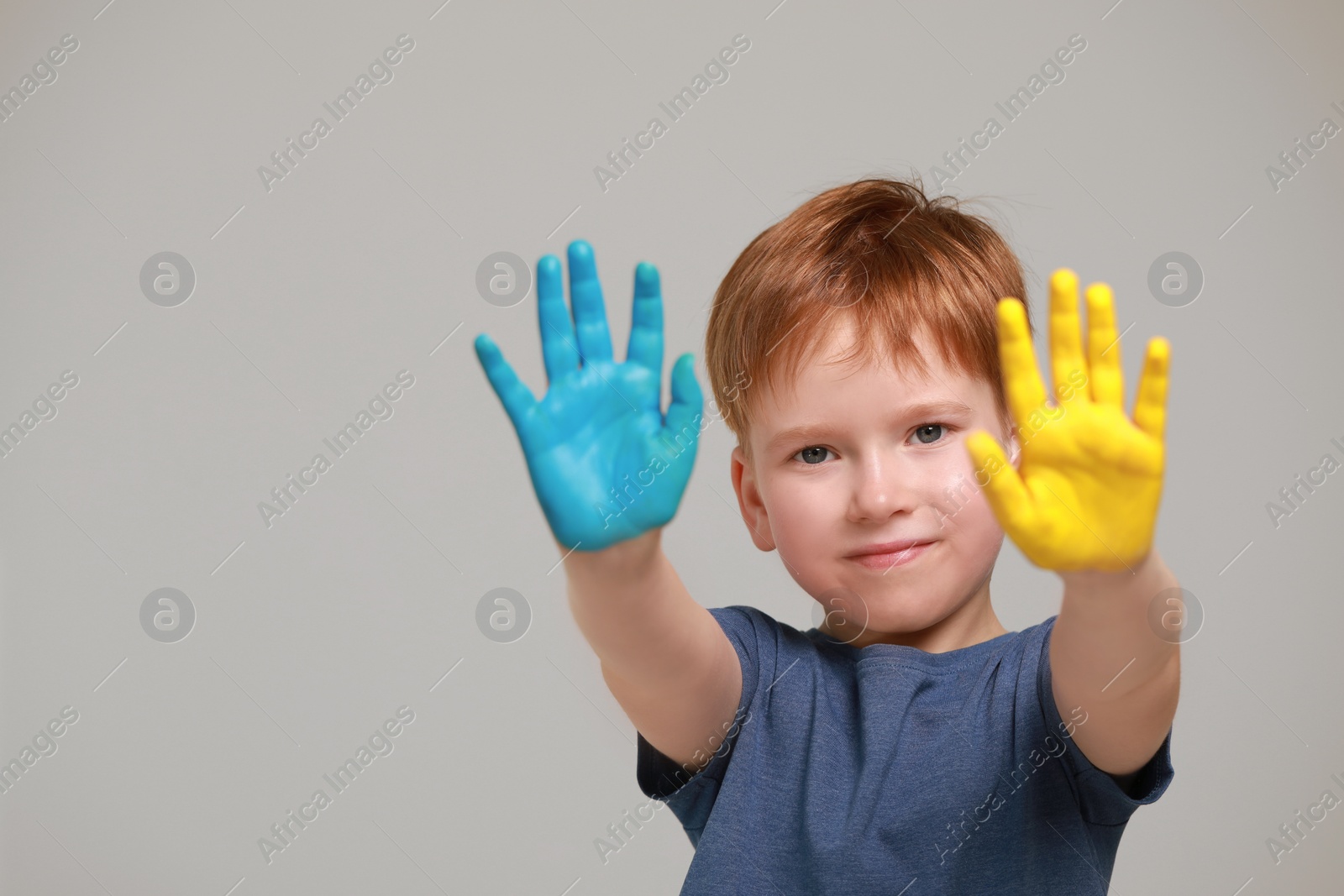 Photo of Little boy with hands painted in Ukrainian flag colors on light grey background, space for text. Love Ukraine concept