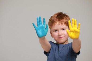 Photo of Little boy with hands painted in Ukrainian flag colors on light grey background, space for text. Love Ukraine concept