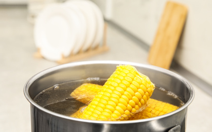Photo of Pot with boiling corn in kitchen, closeup