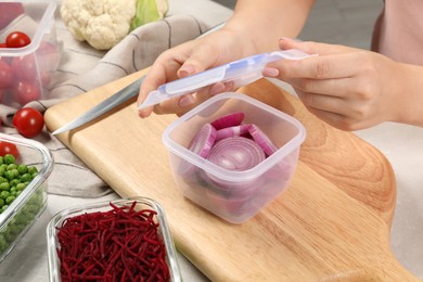 Woman closing plastic container with lid at table, closeup. Food storage
