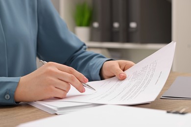Woman signing document at wooden table, closeup