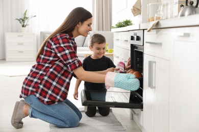 Photo of Son and mother taking out tray of baked buns from oven in kitchen