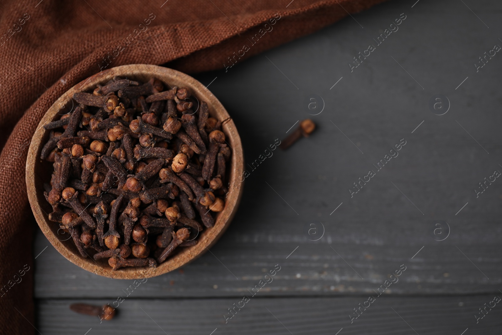 Photo of Aromatic cloves in bowl on grey wooden table, top view. Space for text