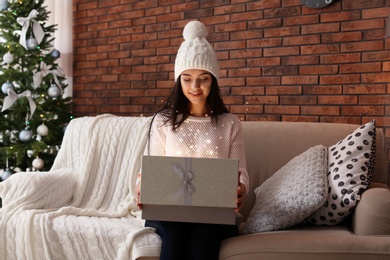 Photo of Beautiful young woman in hat opening gift box at home. Christmas celebration