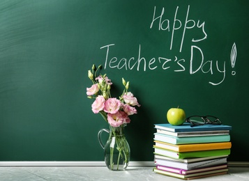 Photo of Green chalkboard with inscription HAPPY TEACHER'S DAY, vase of flowers and books on grey stone table. Space for text