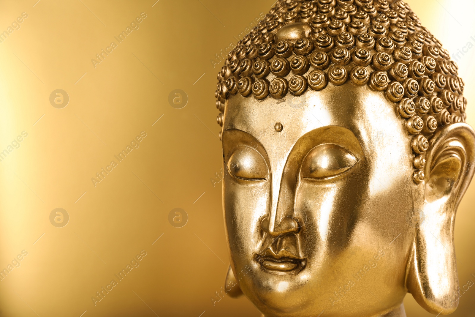 Photo of Buddha statue on golden background, closeup. Space for text