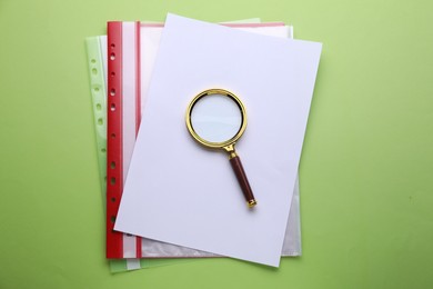 Magnifying glass and folders with paper sheets on light green background, top view