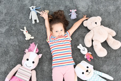 Photo of Cute little girl and soft toys on floor, top view