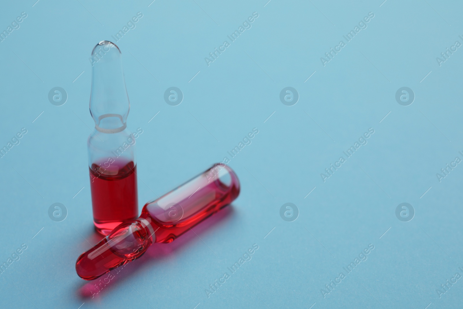 Photo of Two medical ampoules with solution on light blue background. Space for text