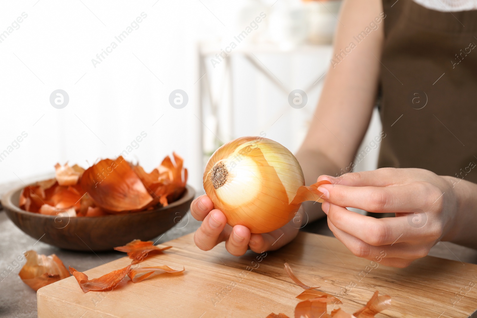 Photo of Woman peeling ripe onion at table, closeup