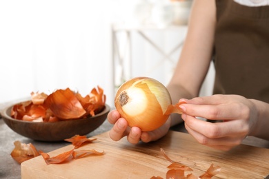 Photo of Woman peeling ripe onion at table, closeup