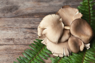 Delicious organic oyster mushrooms with leaves on wooden background, space for text