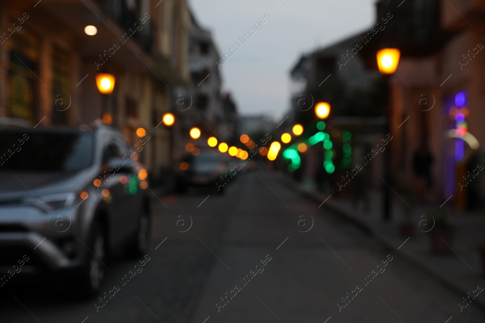 Photo of Blurred view of city street with parked cars in evening