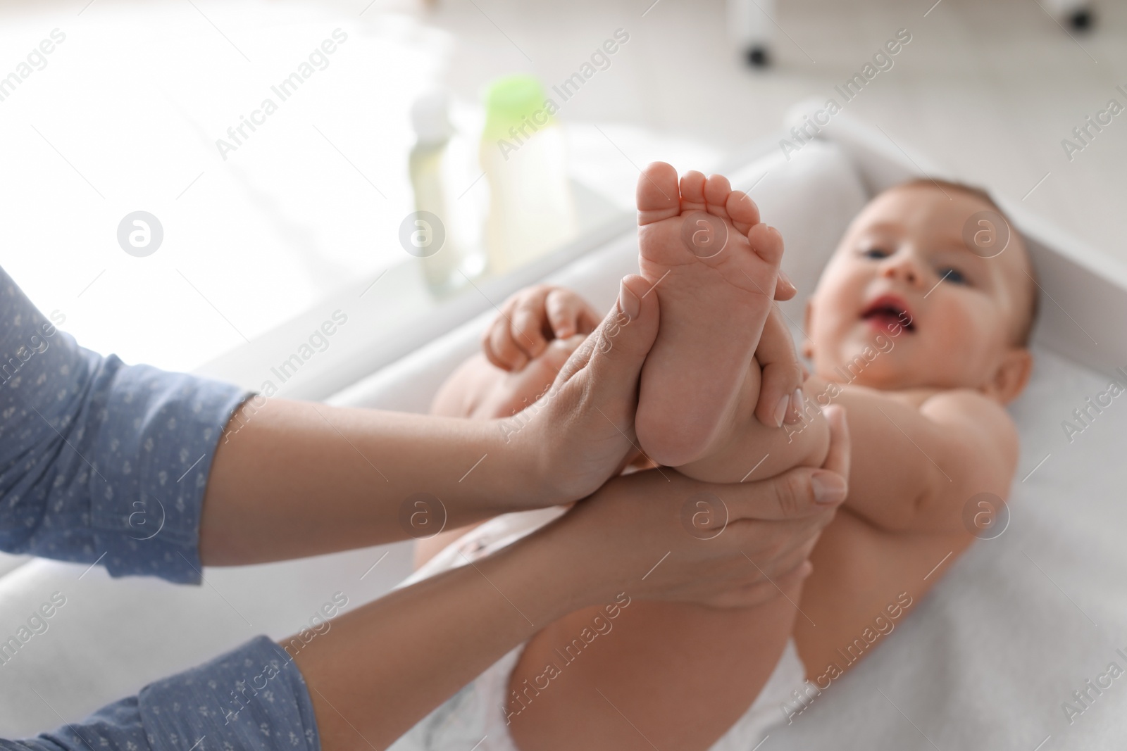 Photo of Mother massaging her baby with oil on changing table at home, closeup