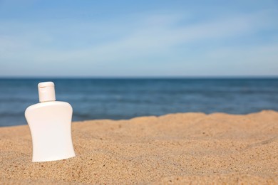 Photo of Blank white bottle of sunscreen on sand near sea, space for text