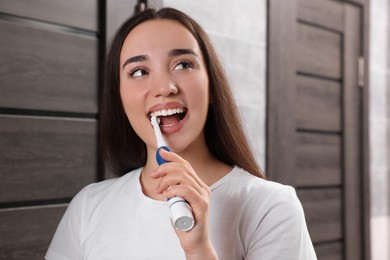 Photo of Young woman brushing her teeth with electric toothbrush in bathroom