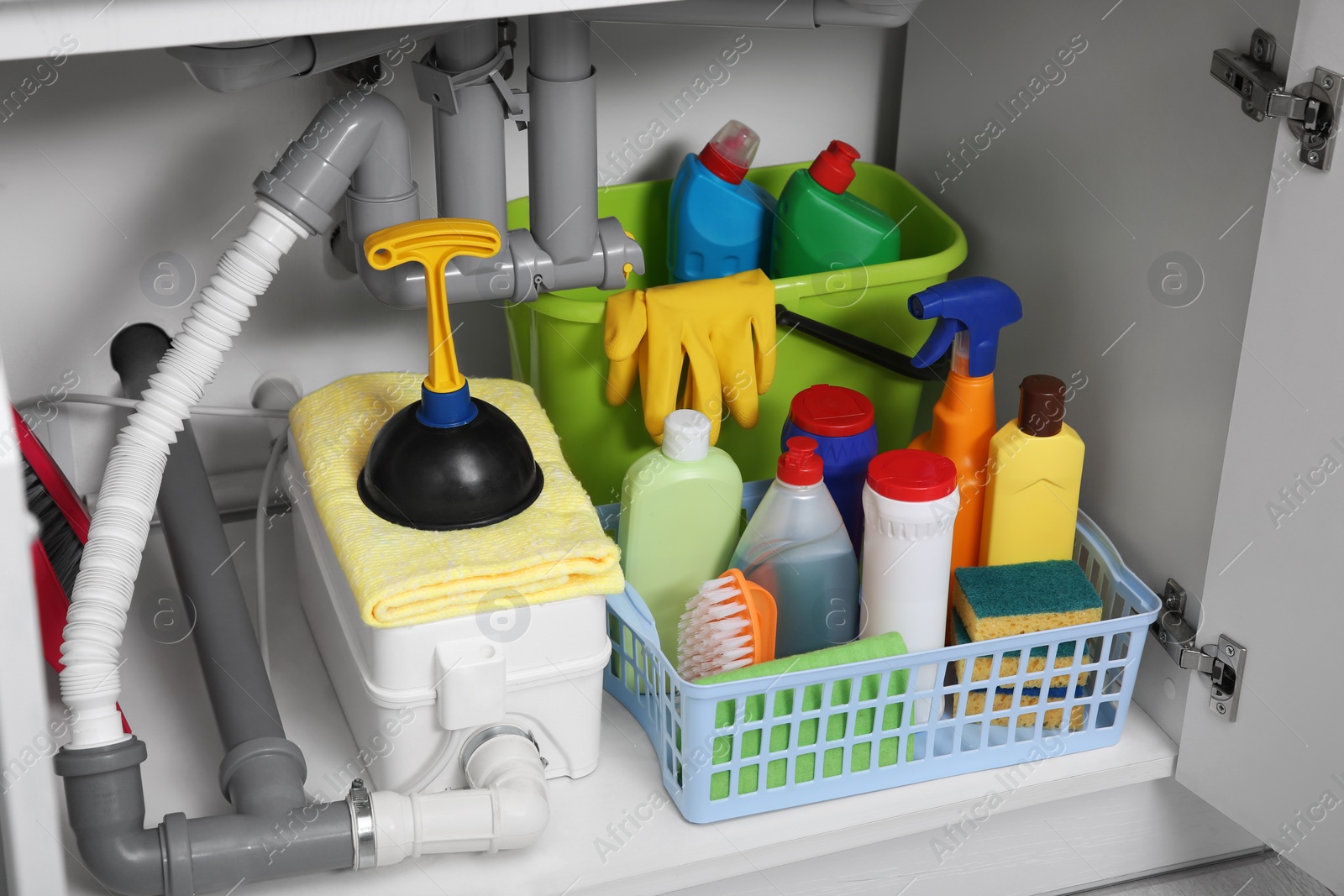 Photo of Open under sink cabinet with different cleaning supplies in kitchen