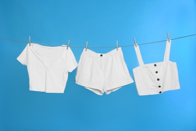 Different clothes drying on laundry line against light blue background