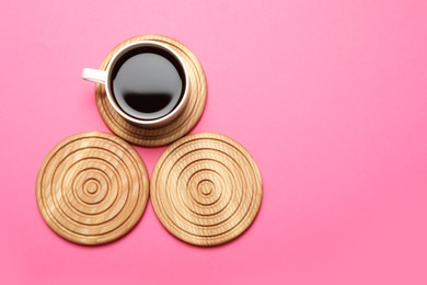 Photo of Cup of coffee and stylish wooden coasters on pink background, flat lay. Space for text
