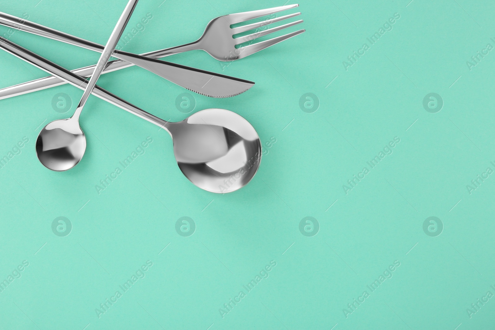 Photo of Fork, knife and spoons on turquoise background, flat lay with space for text. Stylish cutlery set