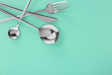 Photo of Fork, knife and spoons on turquoise background, flat lay with space for text. Stylish cutlery set