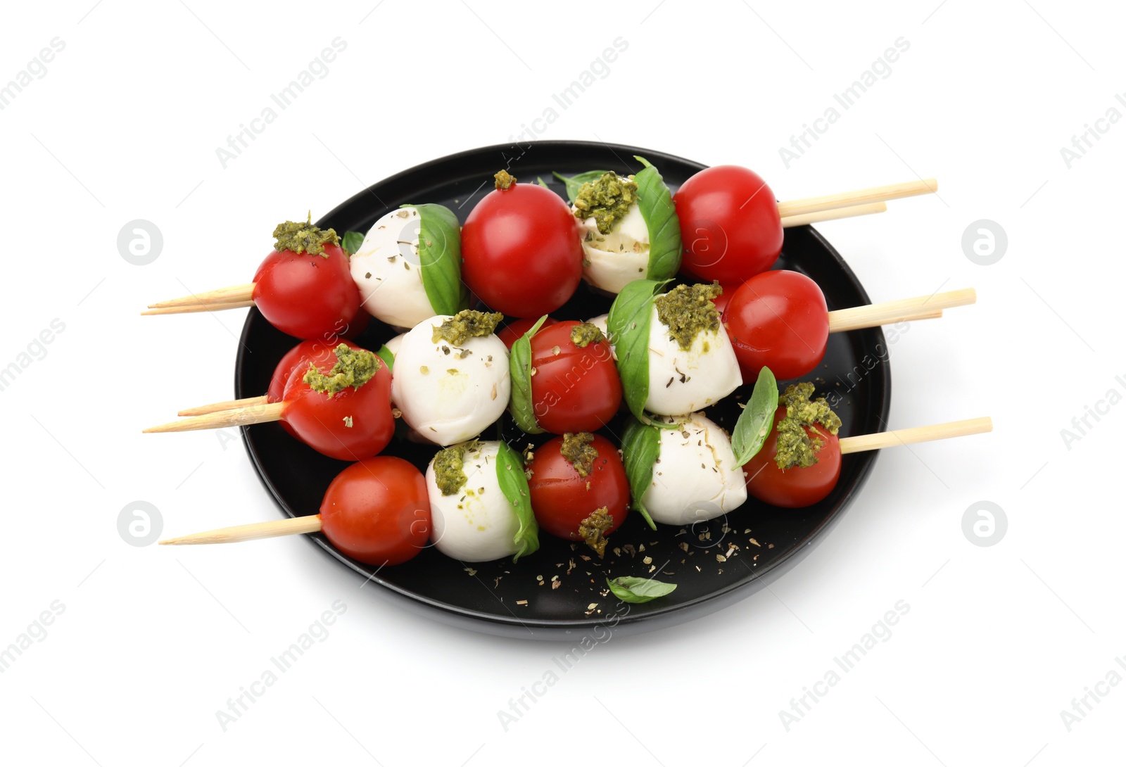 Photo of Plate of Caprese skewers with tomatoes, mozzarella balls, basil and pesto sauce isolated on white